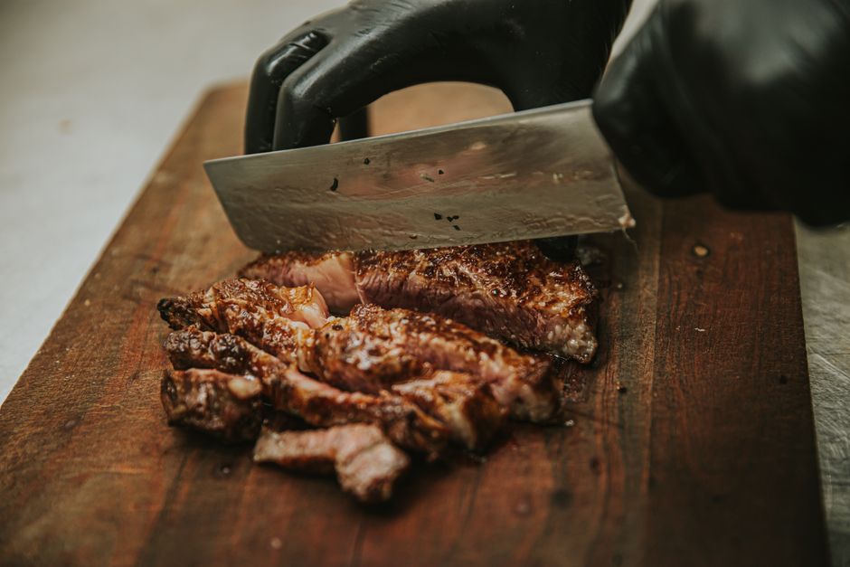 Close-up of chef slicing juicy grilled steak on wooden cutting board with cleaver.